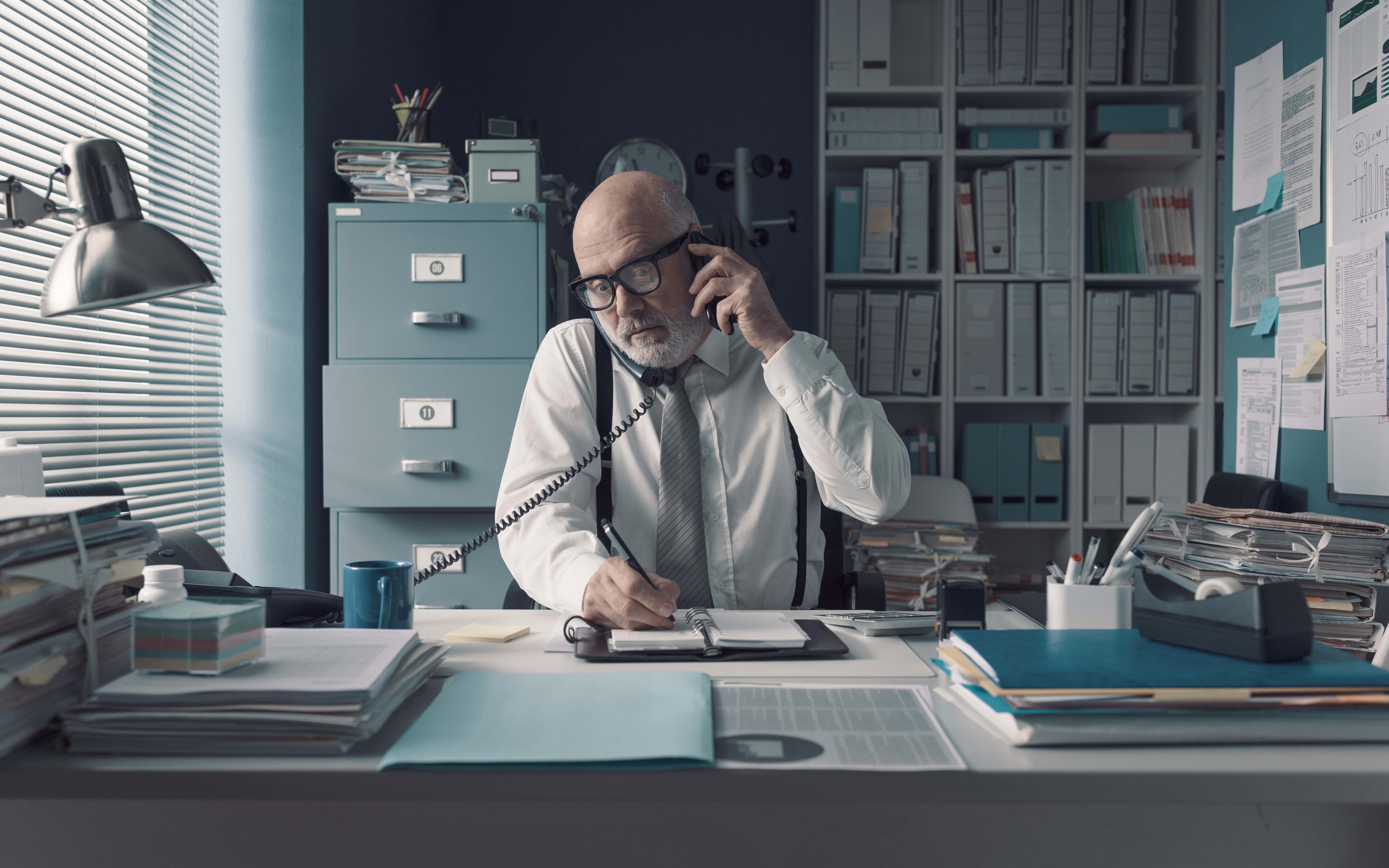 A professional managing call and writing memo exposes isolation of phone systems from essential software